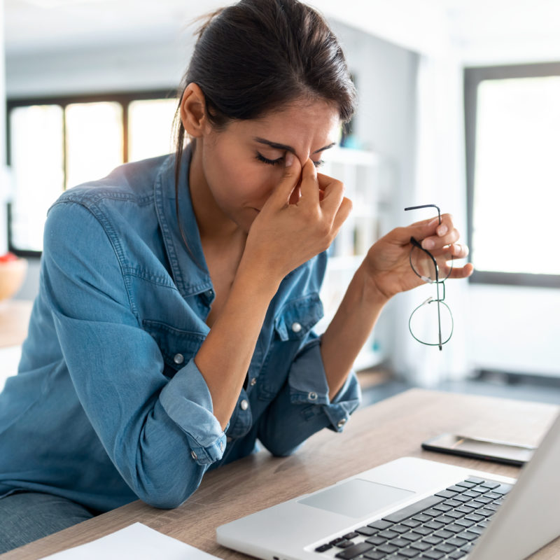 stressed woman pinching her nose and holding glasses while working